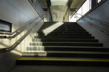 Gölge aydınlatmalı metal tırabzanlar olan bir yeraltı geçidinde adımlara dikkat edin.