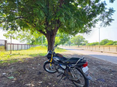 Gulbarga, Hindistan- 26 Kasım 2022, demirhindi ağacının gölgesinde park etmiş Hero Honda Splender bisikletinin stok fotoğrafı. Güneşli bir öğleden sonra çekilmiş bir resim. seçici odak.