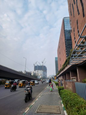 Hyderabad, Hindistan - 6 Ocak 2023; IT şirketi veya yazılım şirketinin dışında, insanlar bina yakınında boş bir yolda yürüyorlar. Araçlar asfalt yolda ilerliyor. Yeni inşaat çalışmaları devam ediyor..