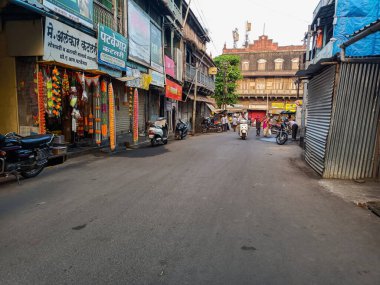 Kolhapur, Hindistan - 6 Kasım 2022; Pazar alanı boyunca, asfalt üzerinde park halindeki araçların arasında scooter süren bir adam ortaya çıktı. Bazı dükkanlar açık kalırken, diğerleri kapalı kaldı.