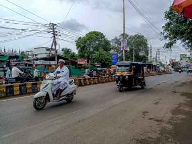 Gulbarga, Hindistan - 19 Temmuz 2024 kalabalık Hint şehir yolunda, 60-70 yaş arası büyükbaba, geleneksel beyaz giyimli ve şapkalı, motosikletli, otomobil tribünleri ve diğer araçlarla çevrili..