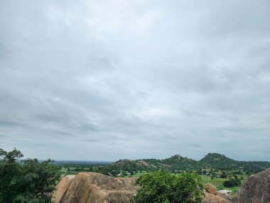 Geniş açılı, göz hizasında kırsal bir manzara. Yuvarlanan tepeler, yemyeşil bitkiler ve bulutlu bir gökyüzünün altındaki kayalık çıkıntılar. yayılmış ışık ve sessiz renkler huzur ve doğal atmosfer yaratır.