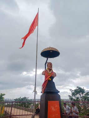 Kolhapur, Hindistan 26 Haziran 2024 Chhatrapati Shivaji Maharaj 'ın çelenk ve safran kumaşla süslenmiş heykeli, gökyüzü bulutlu bir tepede safran bayrağının yanına yerleştirilmiş.