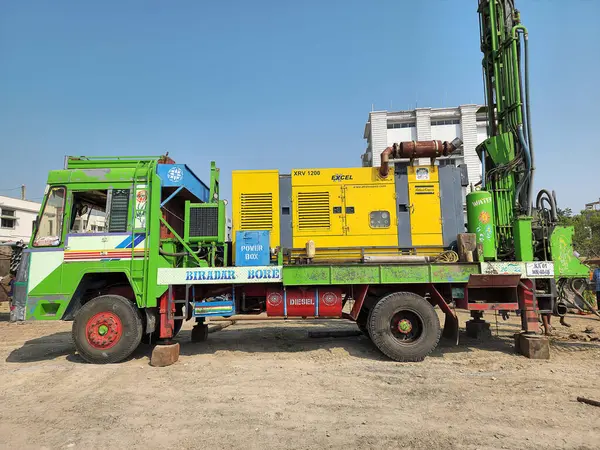 Gulbarga, Hindistan, 21 Aralık 2023 Renkli Borewell sondaj kamyonu tozlu bir alana park edilmiş, büyük sarı bir Atlas ve yeşil sondaj sondaj teçhizatı ile donatılmış, yeraltı su çıkarma çalışması için hazır.
