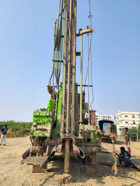 Gulbarga, Hindistan, 23 Şubat 2023; İşçiler bir kamyona monte edilmiş devasa yeşil ve sarı bir borewell sondaj makinesi kullanıyorlar. Parlak gökyüzünün altındaki tozlu ve açık bir alanda ekip endüstriyel su sondajı projesinde birlikte çalışıyor..