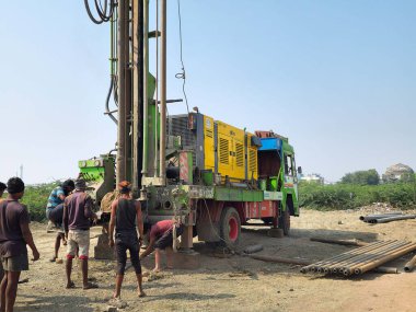 Gulbarga, Hindistan, 23 Şubat 2023; İşçiler bir kamyona monte edilmiş devasa yeşil ve sarı bir borewell sondaj makinesi kullanıyorlar. Parlak gökyüzünün altındaki tozlu ve açık bir alanda ekip endüstriyel su sondajı projesinde birlikte çalışıyor..