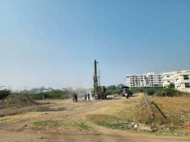 Gulbarga, Hindistan 21 Aralık 2023 Bir sondaj kulesi aktif olarak kuru zemin içine sıkıcı, bir grup işçi tarafından çevrili ve uzak binalar ile açık, parlak bir gökyüzü altında park edilmiş bir kamyon.