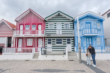 Aveiro, Portekiz - 24.10.2022: Aveiro yakınlarında Costa Nova do Prado adlı tipik renkli çizgili evlerle sokakta selfie çeken aşık bir çift.