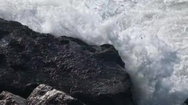 Okyanus dalgaları kıyıdaki kayalara çarpar. Köpüklü ve taş plajlı güzel Atlantik okyanus dalgalarının HD yavaş çekim görüntüsü. Yüksek kaliteli FullHD görüntüler.