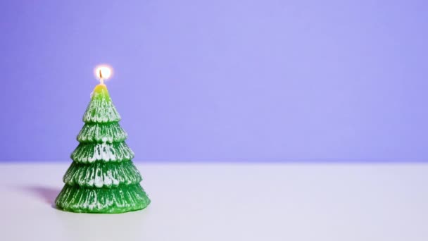 ライラックの背景に燃える緑のクリスマスツリーワックスキャンドル コピースペース付きの新年やクリスマスビデオバナー — ストック動画