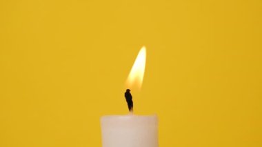 Sarı arka planda beyaz bir mum. Bir mum yanıyor. 4K çözünürlük videosu.