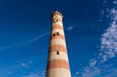 Eski çizgili deniz feneri ve mavi gökyüzü manzarası. Deniz fenerinin ana amacı seyir yardımı için bir yol gösterici olarak hizmet etmektir.
