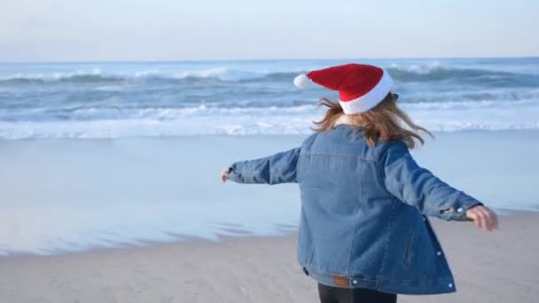 산타클로스 모자를 소녀나젊은 서양의 바닷가를 뛰어다니며 뛰어다니며 재미있게 크리스마스나 해상도 — 비디오