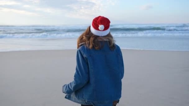 赤いサンタクロースの帽子の女の子や若い女性は ビーチ大西洋を走ったり回ったりして楽しんでいます クリスマスまたは新年の休日の概念 4K解像度ビデオ — ストック動画
