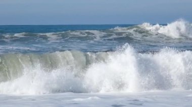 Atlantik Okyanusu 'nun boş sahillerindeki yüksek dalgaların yakın görüntüsü. Dalgalar, deniz köpüğü ve mavi gökyüzü ile dolu boş ve güzel okyanus sahilinin yavaş çekim videosu.