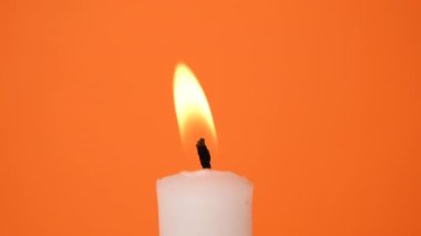 A white candle on an orange background. A candle is burning. 4K resolution video