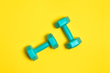 Two bright blue or mint dumbbells are isolated on yellow background. Sport and health concept.
