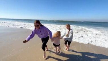 Two daughters and mother are playing with the waves on the beach of the Atlantic Ocean. Family time or vacation concept. 4K resolution video. High quality 4k footage