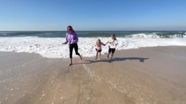 Two daughters and mother are playing with the waves on the beach of the Atlantic Ocean. Family time or vacation concept. High quality 4k footage.