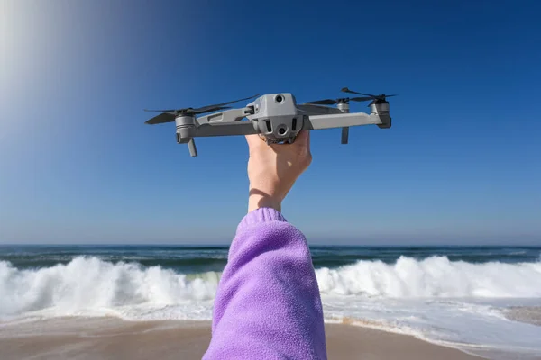 Hand holding drone ready to take off on the background of stormy Atlantic Ocean. Drone in hand.