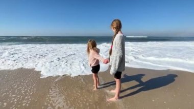 Two little sisters are playing with the waves on the beach of the Atlantic Ocean. Family time or vacation concept. 4K resolution video. High-quality 4k footage