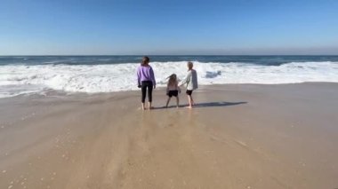 Two daughters and mother are playing with the waves on the beach of the Atlantic Ocean. Family time or vacation concept. High quality 4k footage.