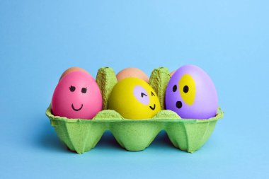Açık mavi arka planda izole edilmiş yeşil kutuda komik yüzlü şirin paskalya yumurtaları. Mutlu Paskalyalar. Boyalı Paskalya yumurtaları.