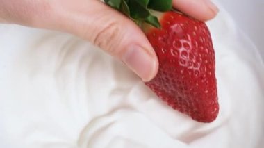 Strawberry dipping in cream, hand dipping berries in milk yogurt, fresh organic dessert. 4K resolution summer food video. Concept of: healthy eating, diet, wellness and strawberries