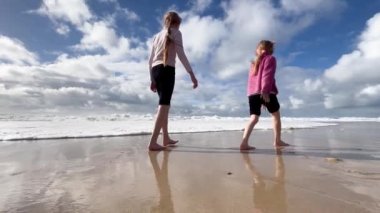 Çocuklar Atlantik Okyanusu kıyısı boyunca koşar. İki küçük kız kardeş Atlantik Okyanusu sahilinde dalgalarla oynuyorlar. Aile zamanı ya da tatil konsepti. 4K çözünürlük videosu.