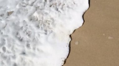 Üst görüntü 4K çözünürlüklü kum, deniz köpüğü ve dalgalı video pankartı. Yazın kumsalda manzaralı plaj ve deniz suyu manzarası. Doğa ve seyahat kavramı.