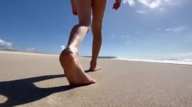 Çocukların ayakları ve bacakları Atlantik Okyanusu sahilinde yalınayak yürüyor ve koşuyor. Dalgaların ve mavi gökyüzünün arka planında Atlantik Okyanusu kıyısında bir çocuk oynuyor. Yüksek kalite 4K görüntü