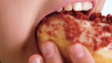 Mutlu bir şekilde çörek yiyen bir çocuğun yakın plan görüntüsü. Bir çocuk donut yiyor. Fast food ve sağlıksız yemek. 4K çözünürlük videosu
