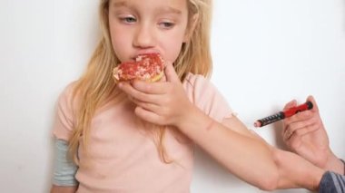 Tip 1 diyabeti olan bir çocuk, annesi koluna insülin enjekte ederken donut yer. Şeker hastası küçük bir kız şeker yiyor..