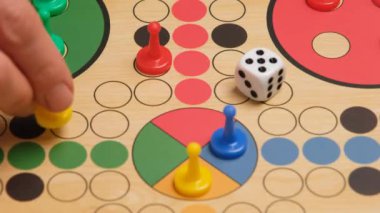 People play Ludo or Pachisi board game on beautiful wooden play board. Ludo is a strategy board game for two to four players. 4K resolution family board game video.
