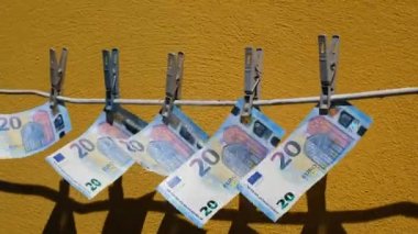 Avro banknotları çamaşır mandallarına asılıp sallanıyor. Sarı duvarın arka planında para rüzgarda sallanıyor. Para aklama kavramı.