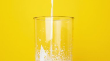 Ev yapımı milkshake yapmak için bardağa süt dökülür. Süt, parlak sarı bir zemin üzerinde mikserden bir bardağa dökülür..