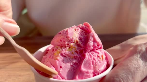 女の子は木製のスプーンで紙コップからピンクのアイスクリームを食べる コーヒーショップのカップでピンクフルーツアイスクリーム — ストック動画