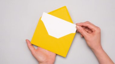 Bir el, parlak sarı bir zarftan beyaz bir kart çıkarır. Gri arkaplandaki sarı zarfın üst görüntüsü. Kopya alanı olan sosyal medya reklamı afişi