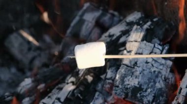Kamp ateşinde kavurulan bir çubuğun üzerindeki şekerlemenin yavaş çekim videosu. Arka planda kamp ateşi olan bir turist marşmelovu kızartıyor. Pişmiş şekerlemenin 4K çözünürlüklü yavaş çekim videosu