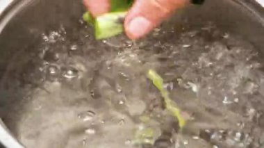 Bir kadın eli, doğranmış yeşil fasulyeyi kaynar suya koyar. Suyun içinde pişen çalı fasulyelerinin yakın plan görüntüsü. Sağlıklı beslenme kavramı.