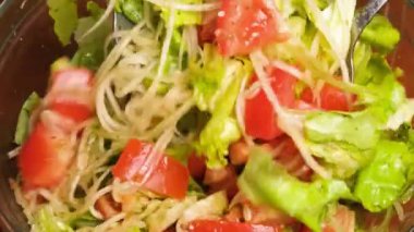 Sebze salatasını karıştıran kadın manzarası. Domates, salatalık, marul ve baharat karışımı sebze salatası. Yemek pişirme videosunun 4K çözünürlüğü.