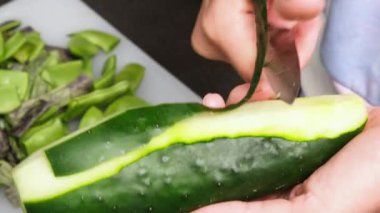 Kadın eli, sebze soyucuyla salatalık soyarken yakından görülüyor. Sağlıklı beslenme kavramı. 4K çözünürlük pişirme videosu