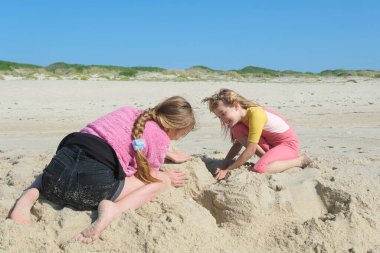 Açık mavi gökyüzünün altında kumdan kale inşa eden iki kız. İki mutlu kardeş Atlantik Okyanusu 'nun ıssız sahillerinde eğleniyor..