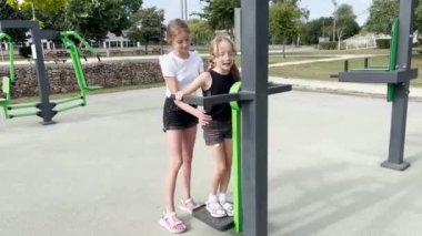 İki kız kardeş spor yapar. Sokakta yaz mevsimi ve çocuklar dışarıda spor salonunda oynuyorlar..
