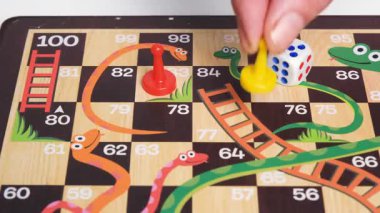 El, sarı oyun taşını renkli masa üzerinde zar ve kırmızı piyon ile hareket ettiriyor. Arkadaş kavramlı masa oyunu zamanı