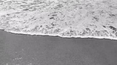 Okyanus dalgalarının kumlu kıyıya vuruşunun gri ölçekli görüntüleri. Köpüklü dalgaların kenarları doğal ritimle dolu sakin ve meditasyon sahnesi yaratır.