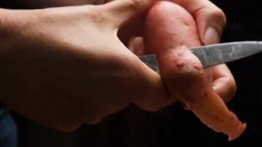 Kırmızı derili patatesi bıçakla soyan bir kadının detaylı görüntüsü. Doğal ışıklandırma, cildin dokusunu ve dikkatli, düzenli yemek hazırlama hareketini vurgular..