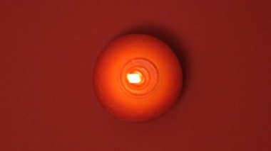 Kırmızı arka planda kırmızı yuvarlak bir mum sakince yanar. Sıcaklığı, romantizmi, meditasyonu ya da canlı monokromatik bir sahnede huzurlu anları temsil eden minimalist yukarıdan aşağıya kompozisyon