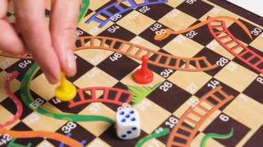 El, sarı oyun taşını renkli masa üzerinde zar ve kırmızı piyon ile hareket ettiriyor. Arkadaş kavramlı masa oyunu zamanı