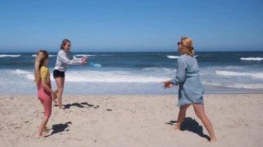 Anne ve iki çocuk sahilde birlikte oynuyorlar, aralarına su dolu bir balon atıyorlar. Neşeli oyun, parlak, güneşli bir gökyüzünün altında okyanus dalgaları tarafından gözler önüne seriliyor.